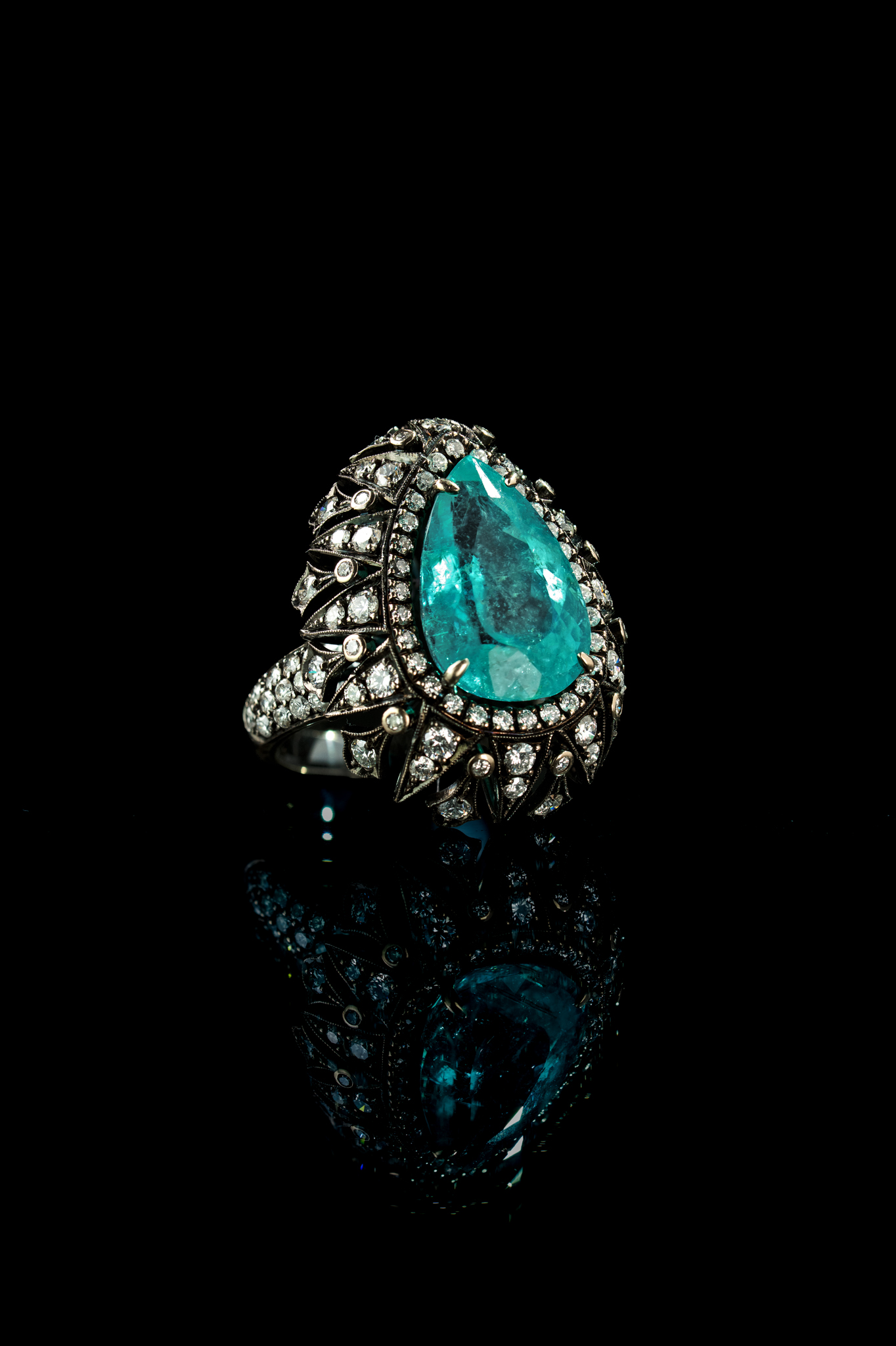 Anel com turmalina Paraíba e diamantes sobre fundo preto com reflexo